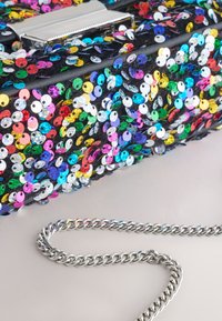 Juoda rankinė, padengta įvairiaspalvėmis apvalių blizgučių sekomis, su sidabrine grandinėlės petneša ir metaline sagtimi. Tekstūruota paviršius su ryškiais raštais.