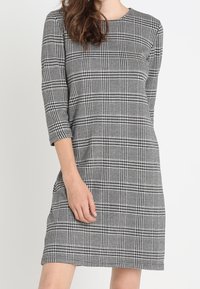 SVART OCH VIT RUTIG KLÄNNING MED TREKVARTSLÅNGA ÄRMAR, RUND NACKÖPPNING OCH RAK SKÄRNING. MJUKT, TEXTURERAT TYG UTAN STÄNGNINGAR.