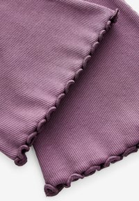 Tissu côtelé et texturé en violet doux avec des bords festonnés. Le matériau semble extensible et léger, conçu pour le confort.