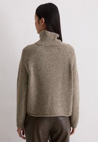 Beżowy, textured oversize sweter z wysokim żeberkowym kołnierzem. Posiada luźny krój, długie rękawy i subtelne kolorowe smugki w całym wyrobie.