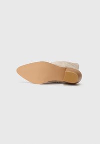 Botte cheville en daim beige avec un bout arrondi et lisse, ainsi qu'une semelle en caoutchouc légère. Dispose d'un talon modeste et d'une semelle intérieure texturée pour une bonne adhérence.