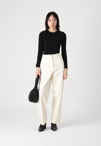 Černý dlouhý rukáv, bílé široké kalhoty, černá pletená kabelka a černé lodičky. Jednoduchý, elegantní design s neutrální barevnou paletou.