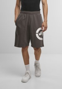 Dark gray shorts with an elastic waistband, side pockets, and a large white graphic design on the left leg. Worn with white sneakers.
