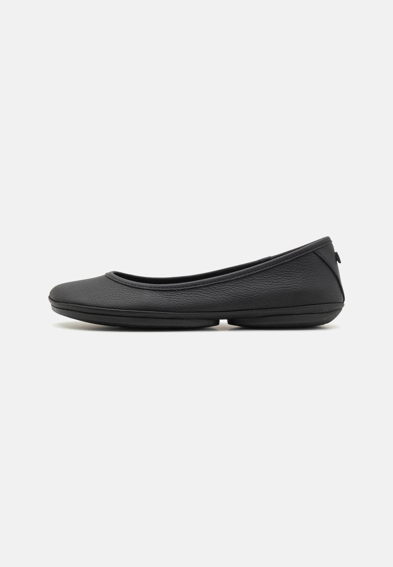 Ballerine en cuir noir avec bout rond, petit talon et semelle lisse, vue de profil sur fond blanc.