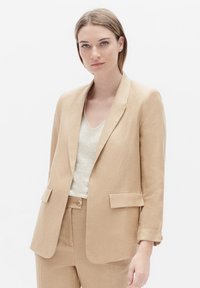 Lichtbeige op maat gemaakte blazer met revers, twee voorzakken en een gladde textuur. Draagt over een lichte top met een klassieke pasvorm.