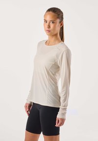 Lichtbeige technische longsleeve met een gestructureerde afwerking, ronde halslijn en een aangesloten pasvorm, gecombineerd met zwarte fietsshorts.