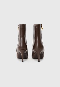 Bottines en cuir marron avec un design épuré, un bout pointu et un talon aiguille. Présentent un accent doré à l'arrière près de la fermeture éclair.