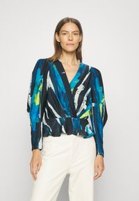 Blus med lång ärm och djup V-ringning, med ett abstrakt mönster i blått, grönt och svart, strukturerad tyg och peplummidja.