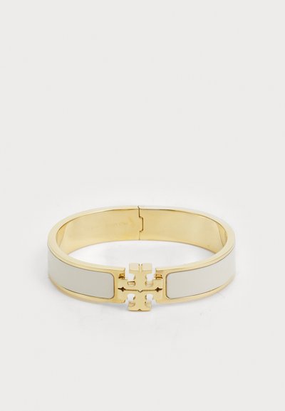 Bracelet jonc en métal doré avec des accents en émail couleur crème et un détail logo signature au centre, texture lisse et forme arrondie.