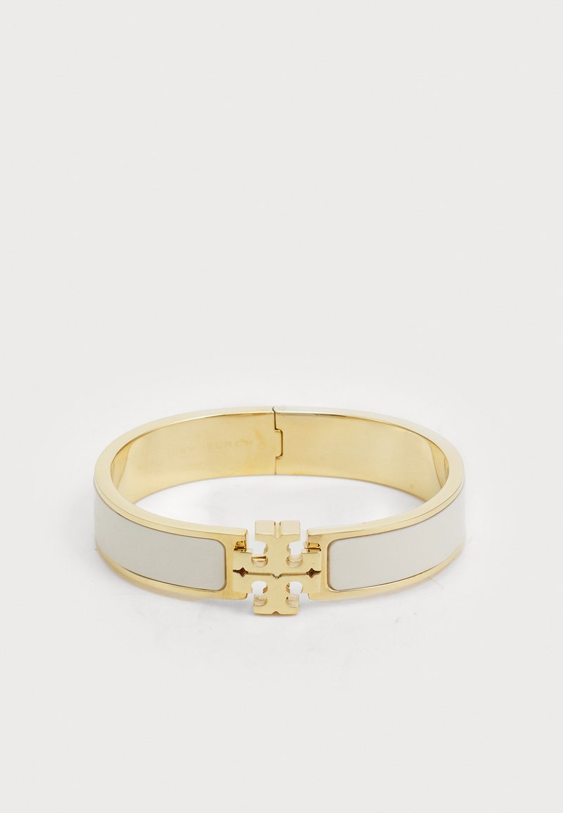 Auksinės spalvos apyrankė su kremine emale ir centre esančiu firminiu logotipu, glotnus paviršius ir suapvalinta forma.