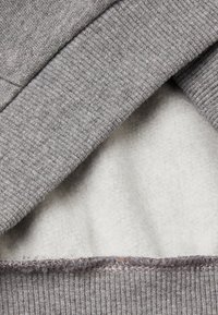 Cuello de sudadera de felpa gris con textura de canalé, mostrando el forro interior esponjoso. Detalle de costura visible a lo largo del borde.