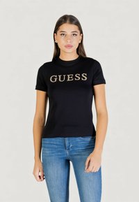 Camiseta de algodón negra con mangas cortas, con un logo "GUESS" brillante en dorado en el pecho. Diseño ajustado con cuello redondo.