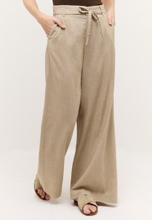 Pantalones de lino beige de pierna ancha con cinturón atado en la cintura, bolsillos laterales, usados con sandalias beige abiertas y camiseta marrón.