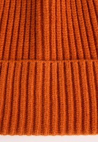 Tissu en tricot côtelé de couleur orange vif, avec une finition texturée comportant des nervures verticales et un ourlet lisse en bas.