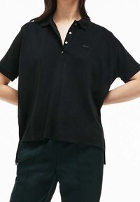 Svart polo skjorta med korta ärmar, utrustad med en tre-knappsslå och en liten broderad logga på bröstet. Tillverkad av texturerat tyg.