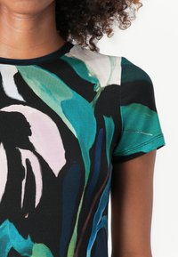 Bunt gestreiftes kurzärmliges Oberteil mit einem floralen Design in Grün-, Schwarz- und Rosatönen. Hergestellt aus glattem, leichtem Stoff mit rundem Ausschnitt.