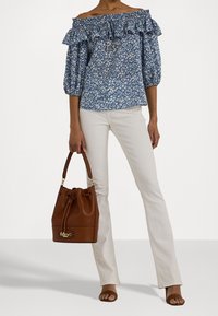 Modrý květinový top bez ramínek s volánovým výstřihem, doplněný smetanovými rozšířenými kalhotami. Hnědá kbelíková taška se zlatými kovovými doplňky.