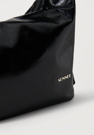 Sac à main noir brillant et souple avec un logo SUNNEI en métal argenté dans le coin inférieur droit sur un fond uni.