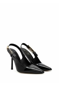 Zapatos de tacón slingback de charol negro con punta afilada, que presentan un detalle de hebilla en tono dorado y un tacón de aguja. Plantilla texturizada.