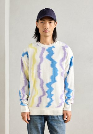 Suéter de punto multicolor con patrones en zigzag en azul, amarillo y morado sobre una base blanca; puños y dobladillo acanalados; corte relajado.