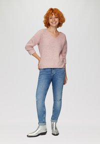 Maglione rosa lavorato a maglia con scollatura a V, con maniche a tre quarti; abbinato a jeans skinny blu e stivaletti alla caviglia metallici argento.