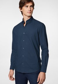 Granatowa koszula z długim rękawem zapinana na guziki z małym białym wzorem w kratkę, z wywiniętym kołnierzykiem i zaokrąglonym dołem. Gładka tekstura tkaniny.