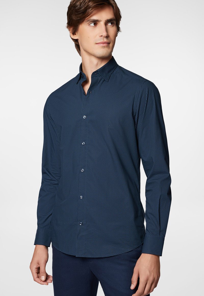 Granatowa koszula z długim rękawem zapinana na guziki z małym białym wzorem w kratkę, z wywiniętym kołnierzykiem i zaokrąglonym dołem. Gładka tekstura tkaniny.