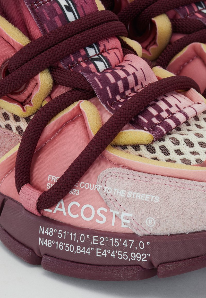 Sneakers Lacoste con parte superiore in rete e camoscio, caratterizzati da una combinazione di colori rosa e bordeaux, motivi elaborati e lacci testurizzati.