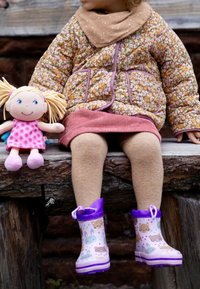 Veste matelassée à fleurs brunes avec des accents roses, jupe en velours côtelé rose, collants beige et bottes en caoutchouc violettes ornées de motifs animaliers. Poupée en peluche à côté.