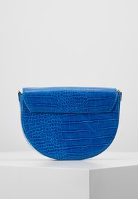 Borsa blu con texture di coccodrillo, dalla forma semicircolare e con chiusura a patta. Presenta una finitura lucida e accessori in metallo.
