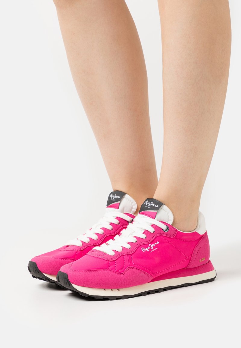 Eldrosa sneakers med vita snören, logotyp på tungan, suède- och tygmaterial, svart gummisula, rund tå och vadderad krage.