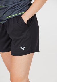 Svarte sportsshorts i en glat tekstur, med et sølvlogo på kanten og lommer på hver side for bekvemmelighed.