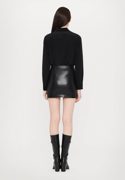 Black long-sleeve shirt paired with a black shiny mini skirt, featuring a fitted silhouette. Knee-high black boots complete the look.
