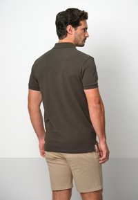 Mörk olivgrön polo med klassisk krage och korta ärmar, tillverkad av slät tyg, ihop med ljusbeiga shorts.
