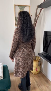 Casaco de estampa de leopardo com cintura cingida, mangas longas e textura suave. Usado sobre calças pretas, com um vaso decorativo dourado ao fundo.