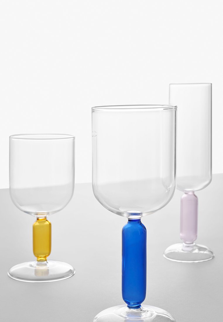 Trzy przezroczyste szklanki z kolorowymi podstawami: jedna żółta, jedna niebieska i jedna fioletowa, o okrągłych kształtach i gładkich powierzchniach.