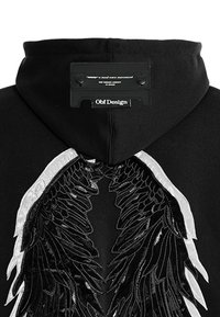 Sudadera negra con un diseño de alas texturizado en plata en la parte posterior. Etiqueta con la marca en la zona del cuello. Tejido suave con un corte casual.