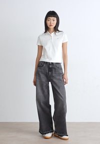 Chemise polo blanche avec un petit logo, assortie à un jean noir taille haute, décontracté et à l'ourlet effiloché. Chaussures : blancs avec des semelles beige clair.