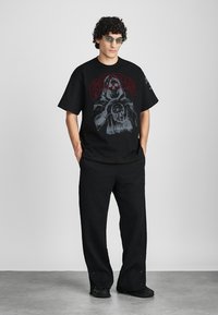 Black graphic t-shirt featuring a bold design with red lettering and a detailed illustration. Paired with textured black wide-leg pants.