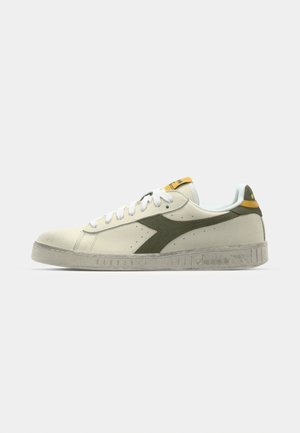 Hvite lær sneakers med grønne semskede detaljer, flat gummisåle, hvite lisser, perforerte detaljer og en gul flik på hælen.