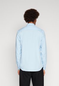 Helles blaues Langarmshirt aus glattem Stoff, mit klassischen Kragen, knöpfbaren Manschetten und einem abgerundeten Saum.