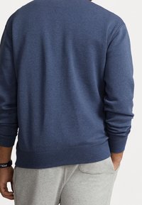 Mörkblå sweatshirt med långa ärmar, ribbade mudd och nederkant, tillverkad av mjukt tyg. Bärs med ljusgrå träningsoverallbyxor.