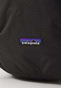 Melna Patagonia soma ar teksturētu virsmu, taisnstūra formu un atpazīstamu daudzkrāsainu kalnu logo uzplecu.