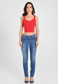 Rotes Cropped-Top mit breiten Trägern, kombiniert mit eng anliegenden blauen Jeans und navyfarbenen High Heels. Einfaches Design, glatte Textur und klassischer Schnitt.