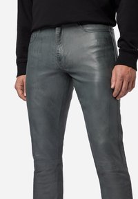 Grijze leren broek met textuur en slim fit, voorzien van een ritssluiting, zijzakken en contrasterende stiksels. Draagt bij aan een casual outfit.