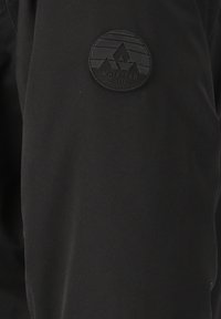 Svart tyg med en slät textur som har en cirkulär, präglad svart logotyp med texten "WHISTLER" och geometriska bergmönster.