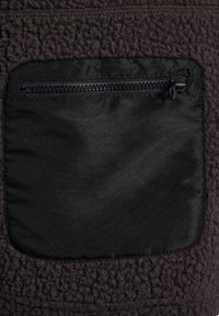 Czarna kwadratowa kieszeń z materiału z zamkiem błyskawicznym na ciemnym, teksturowanym polarze.