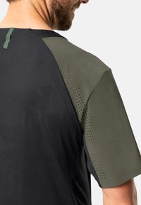 Camisa deportiva de manga corta con un cuerpo negro y acentos en el hombro de color verde oliva, perforados, y tela texturizada para mayor transpirabilidad.