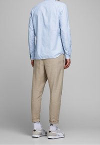 Ljusblå långärmad skjorta, beige tapered byxor, vita sneakers med accenter. Bomullstextur, standard passform, uppvikta byxben.