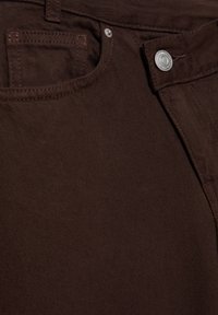 Jeans in denim marrone con una tasca frontale, un bottone metallico e zip. Il tessuto ha una texture liscia con un minimo dettaglio di cucitura.